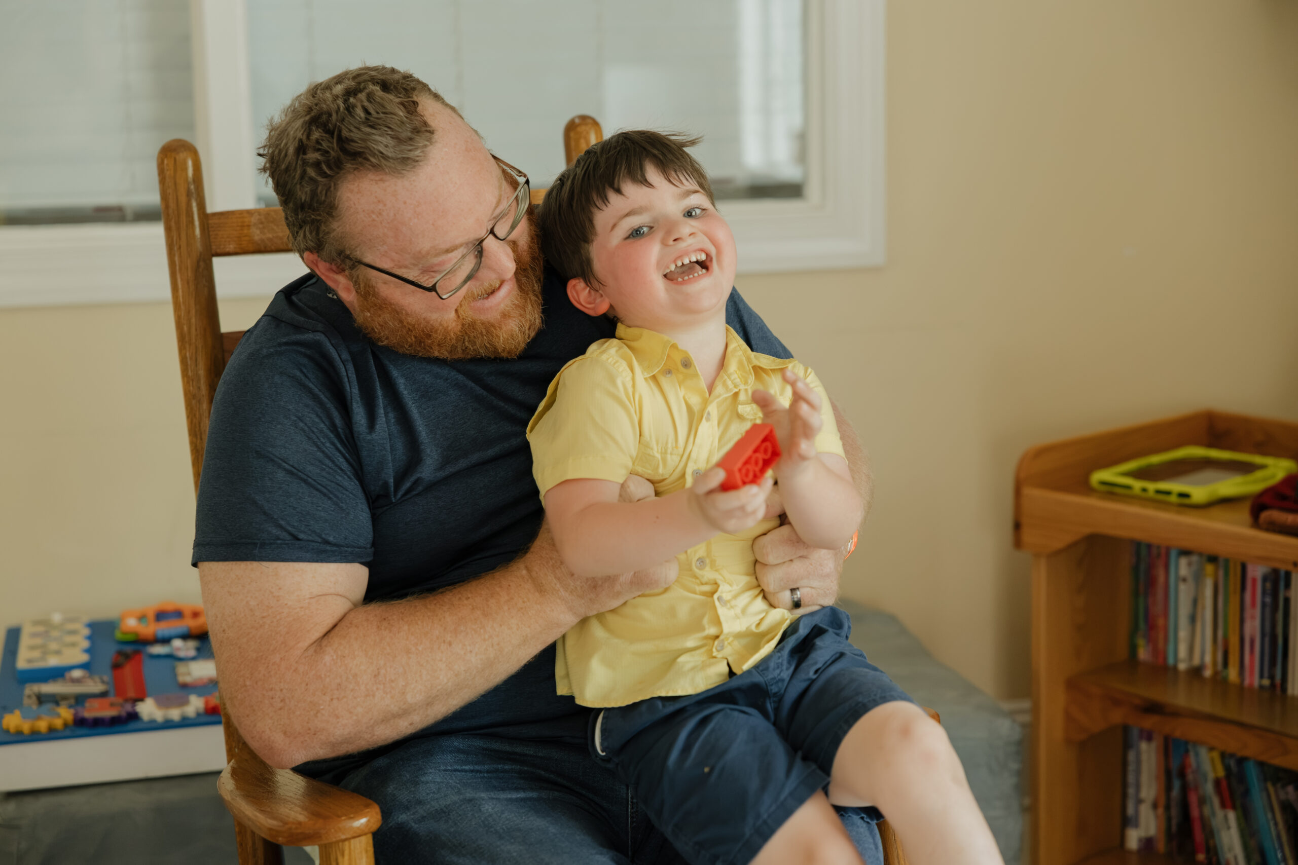 A dad holds his laughing son in his lap
