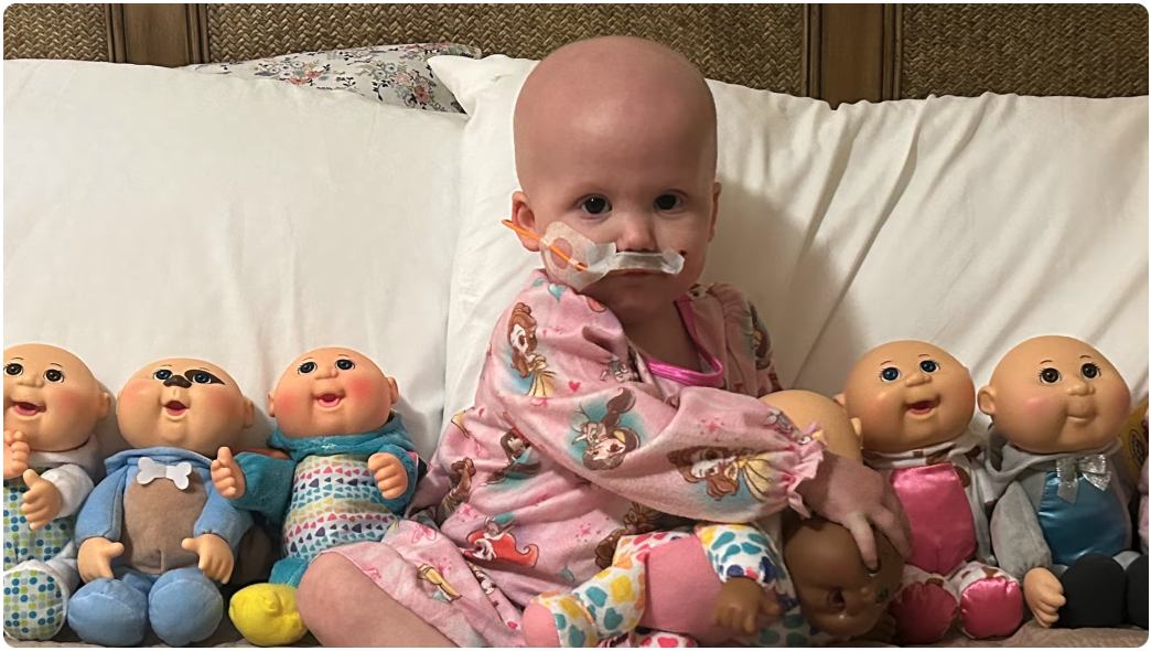 Baby Bristol sitting in a bed surrounded by her dolls.