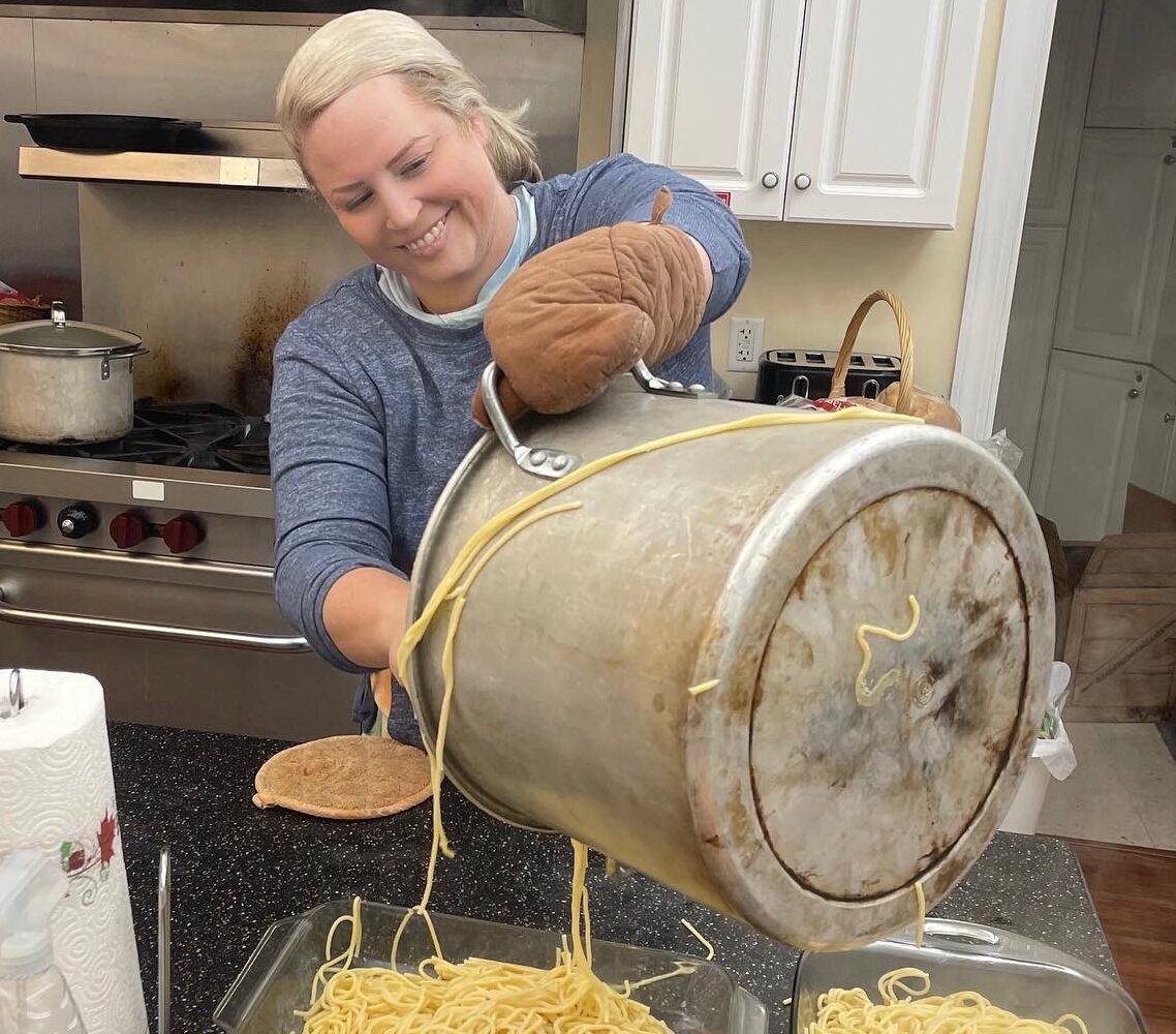 A woman pours freshly cooked noodles into dishes for serving.