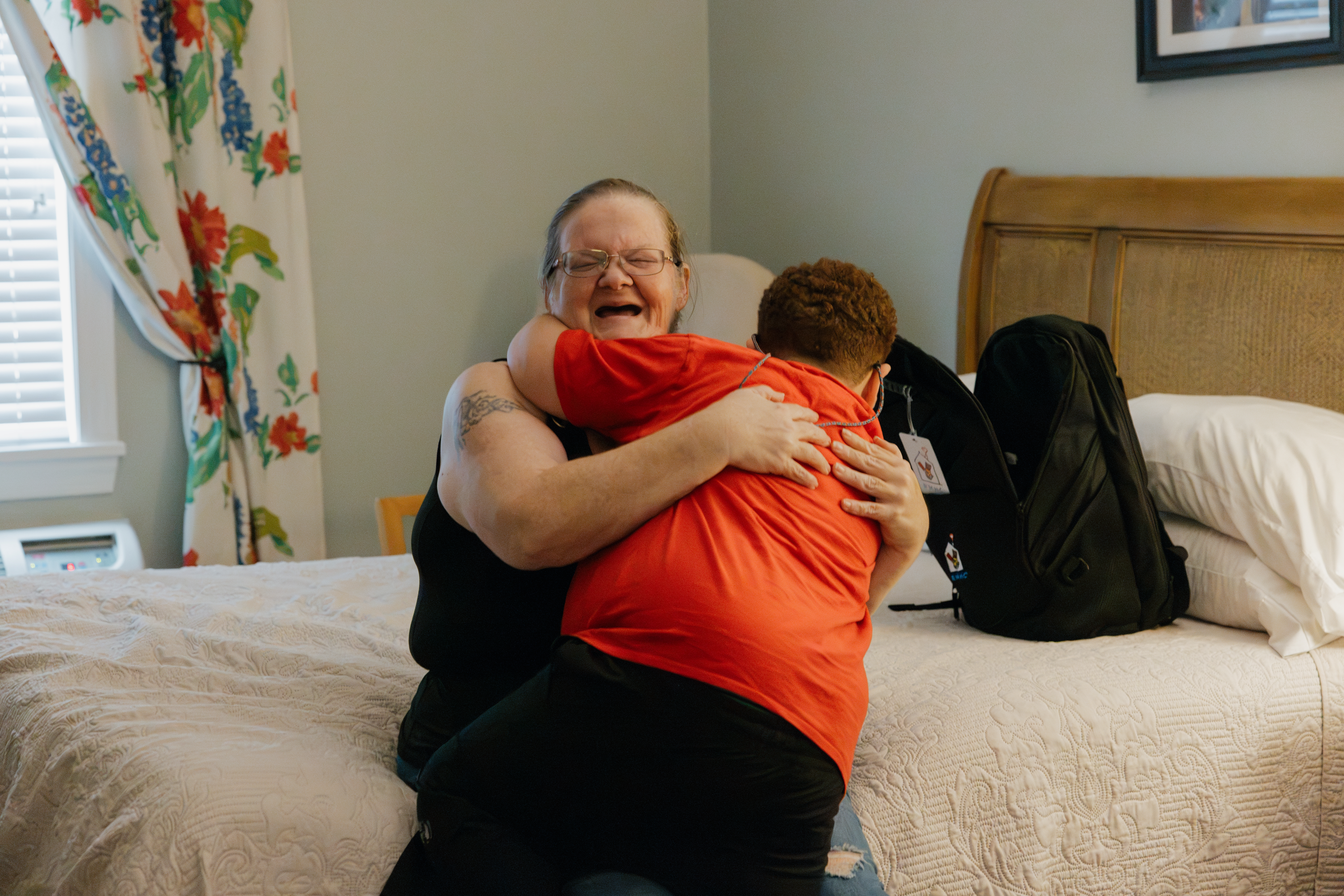 A child hugs his caregiver on a Family Room bed.