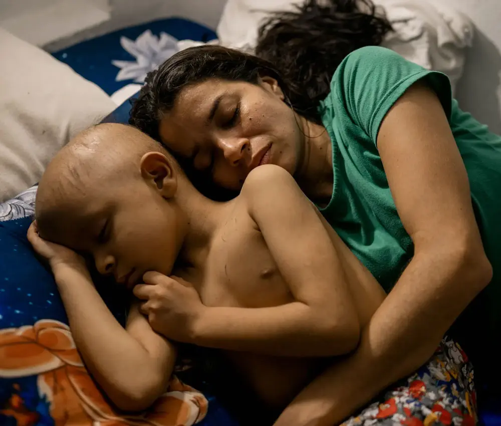 A young mother and child sleep curled up together.