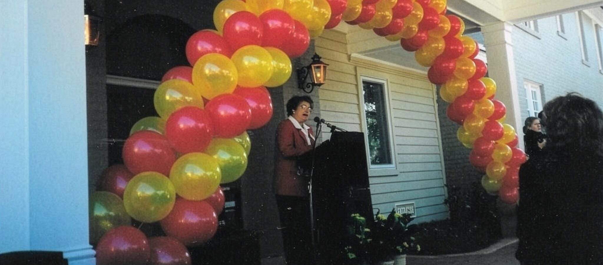 Gray Zimlich speaking at podium under a balloon arch.