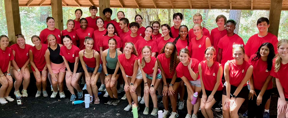 A group of teens pose in their Red Krewe shirts outside at a volunteer event.