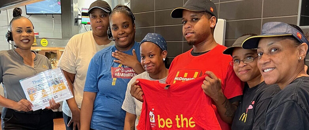 A group of McDonald's employees smile for the camera with various Be the Change signs and shirts.
